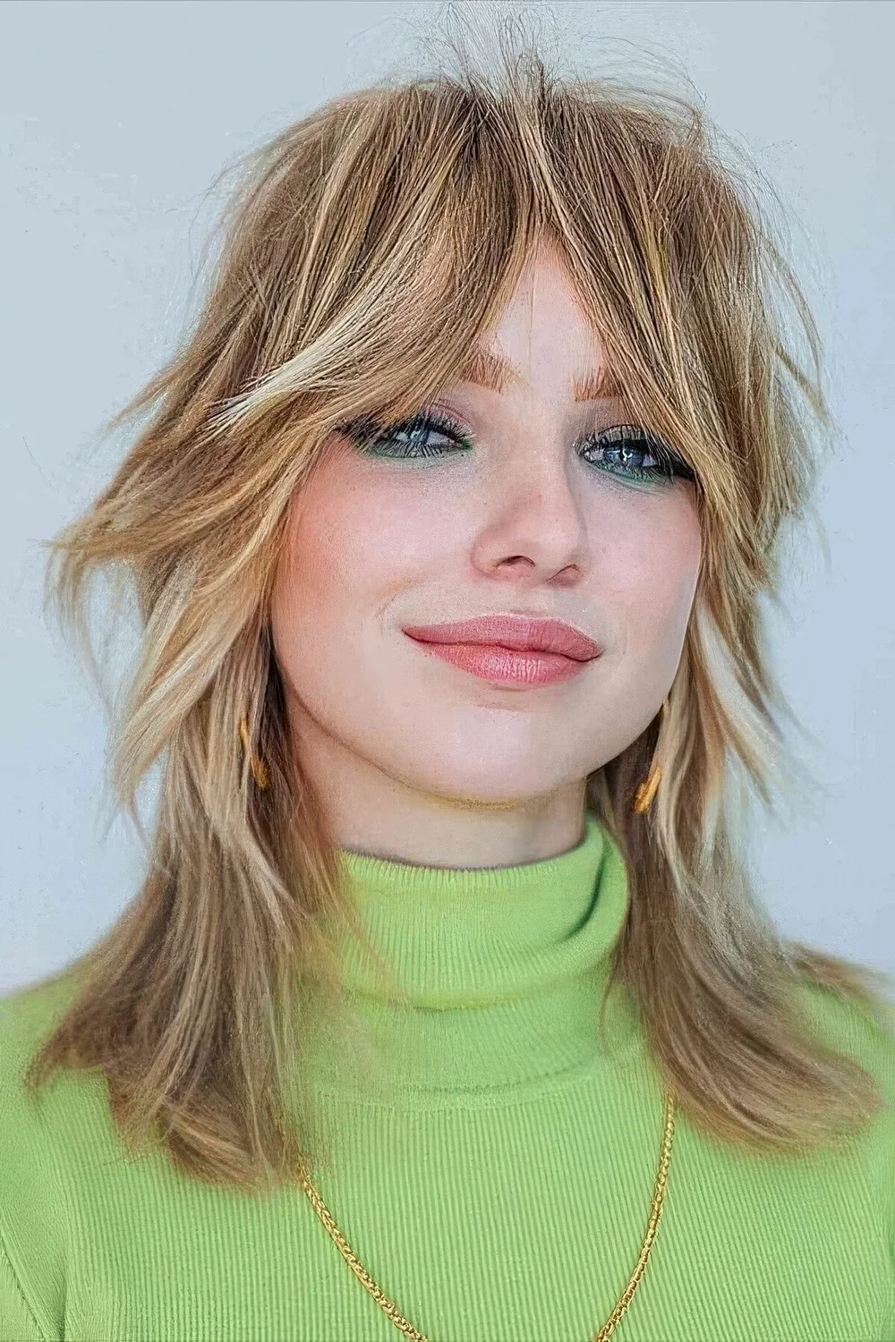 Messy shaggy medium wolf cut with long bottleneck bangs and blonde balayage.