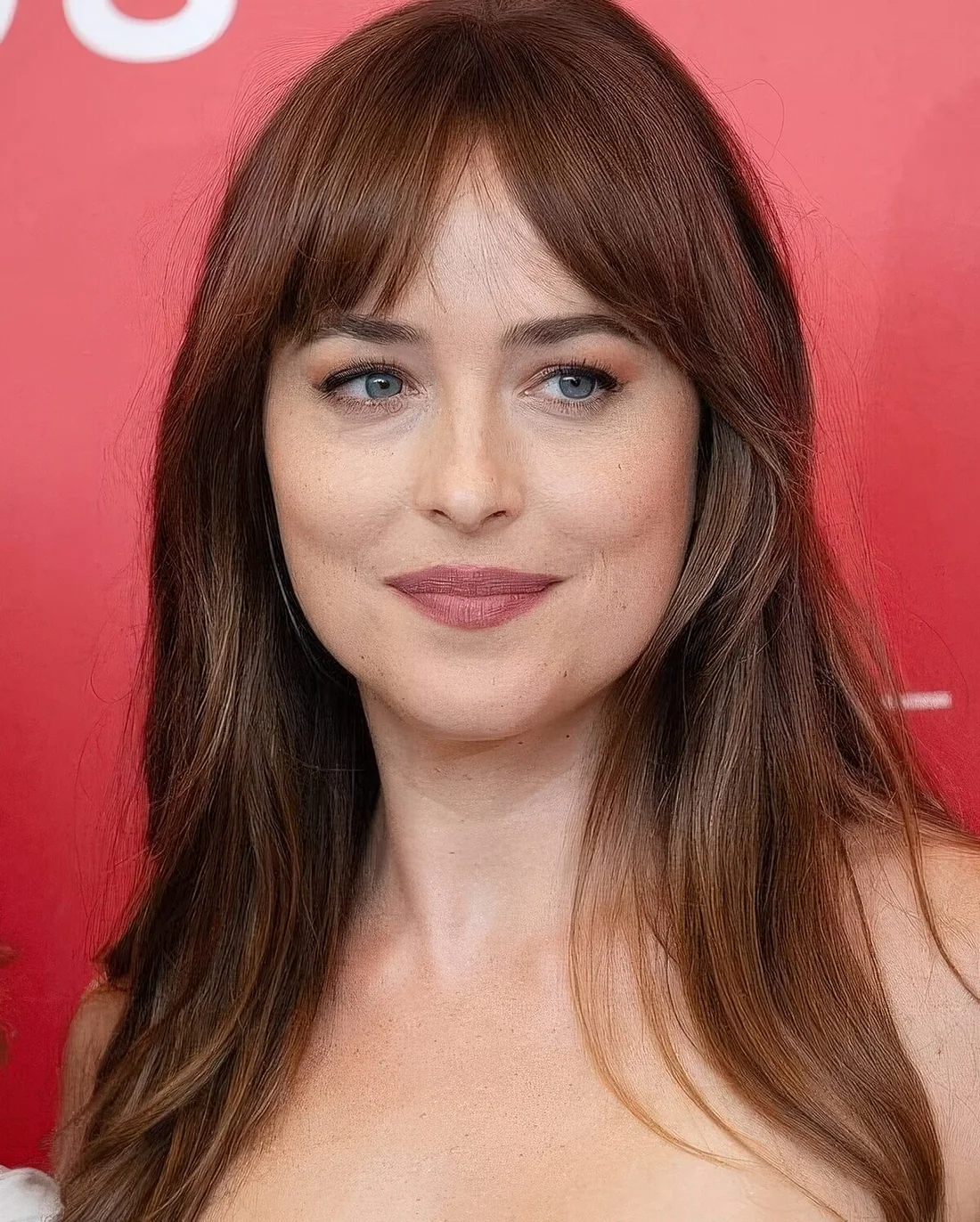Dakota Johnson wearing brunette with a ginger touch hair and bottleneck bangs.
