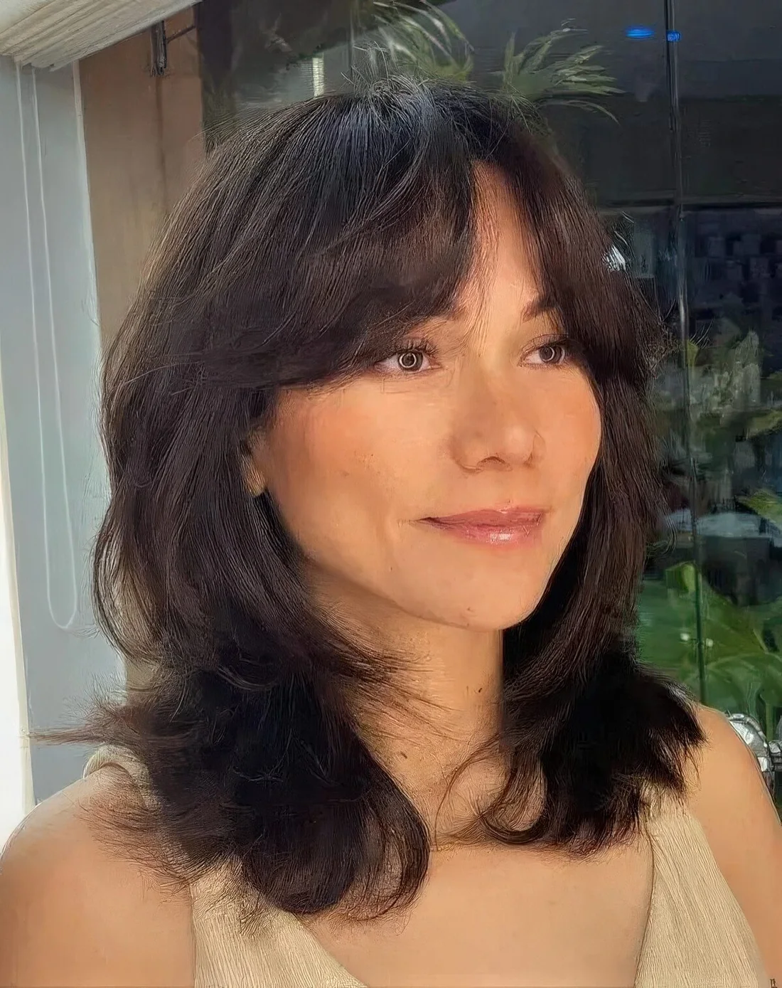Black medium-length butterfly haircut with bottleneck bangs and wavy ends.