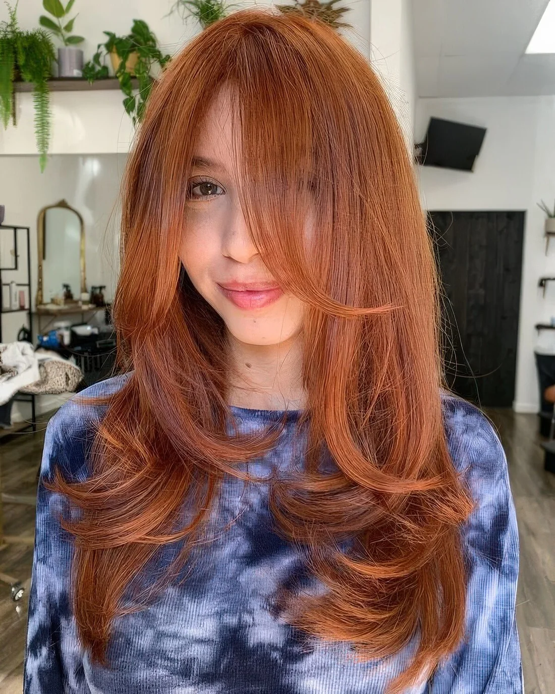 Long and beautiful ginger butterfly haircut with curled ends and bottleneck bangs.