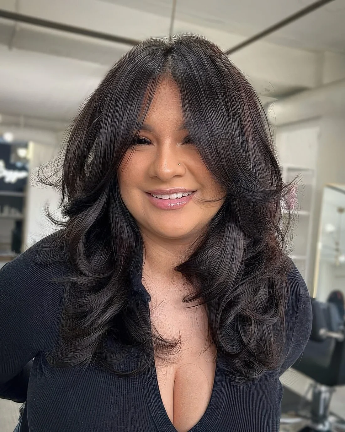 Long black butterfly haircut with auburn highlights and bottleneck bangs and waves plus a lot of dimension.