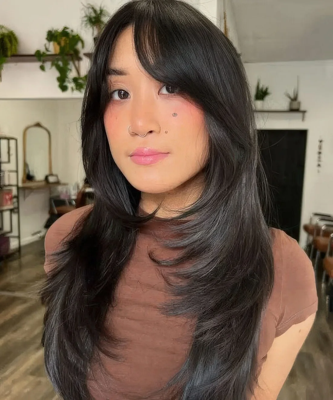 Long black butterfly haircut with bottleneck bangs and curled ends and a shiny touch.