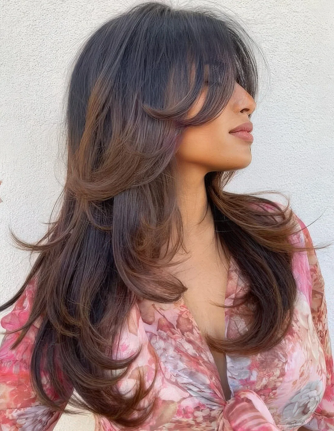 Long black butterfly haircut with brown balayage and bottleneck bangs plus curled ends.