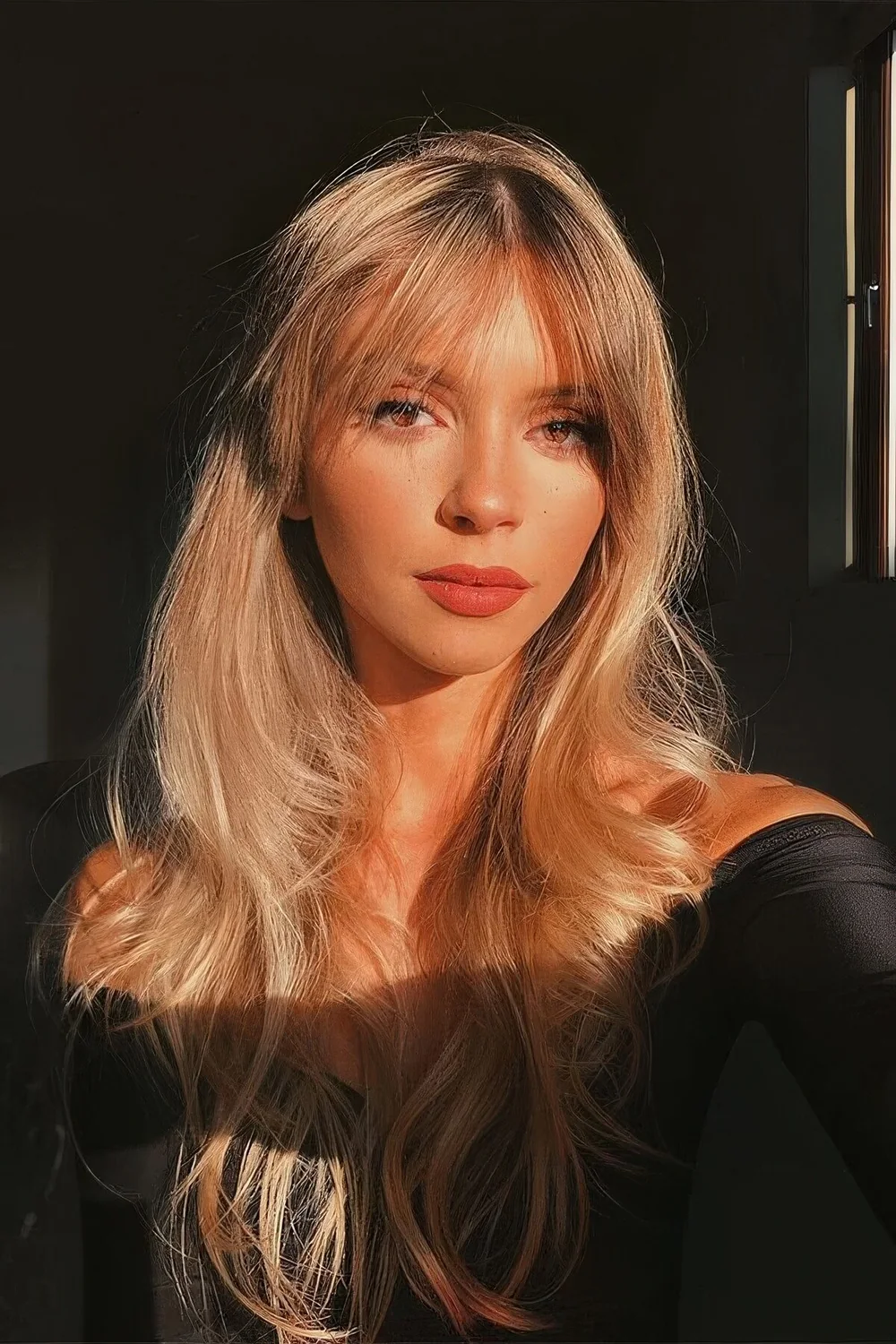 Long blonde butterfly haircut with bottleneck bangs and waves, with a bit of dimension.