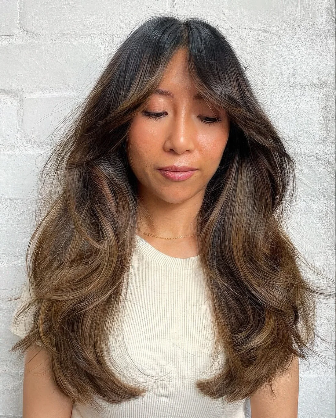 Long dark brunette haircut with bottleneck bangs, dimension and waves plus caramel balayage.