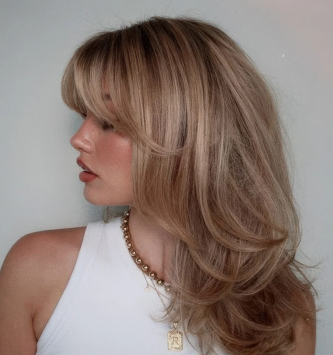 Blonde butterfly haircut with highlights and side and bottleneck bangs.