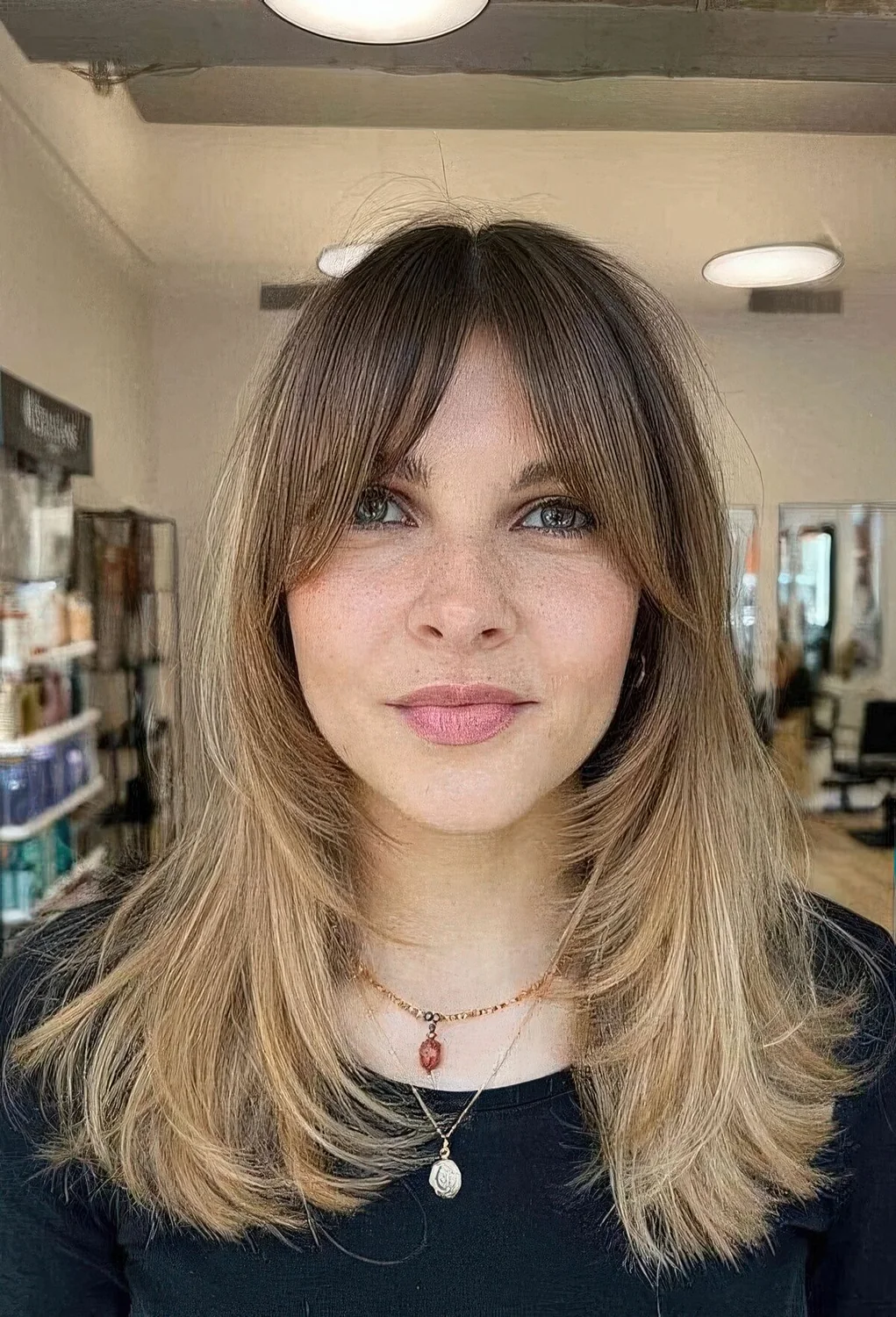 Medium blonde butterfly haircut with a darker root and front plus bottleneck bangs.