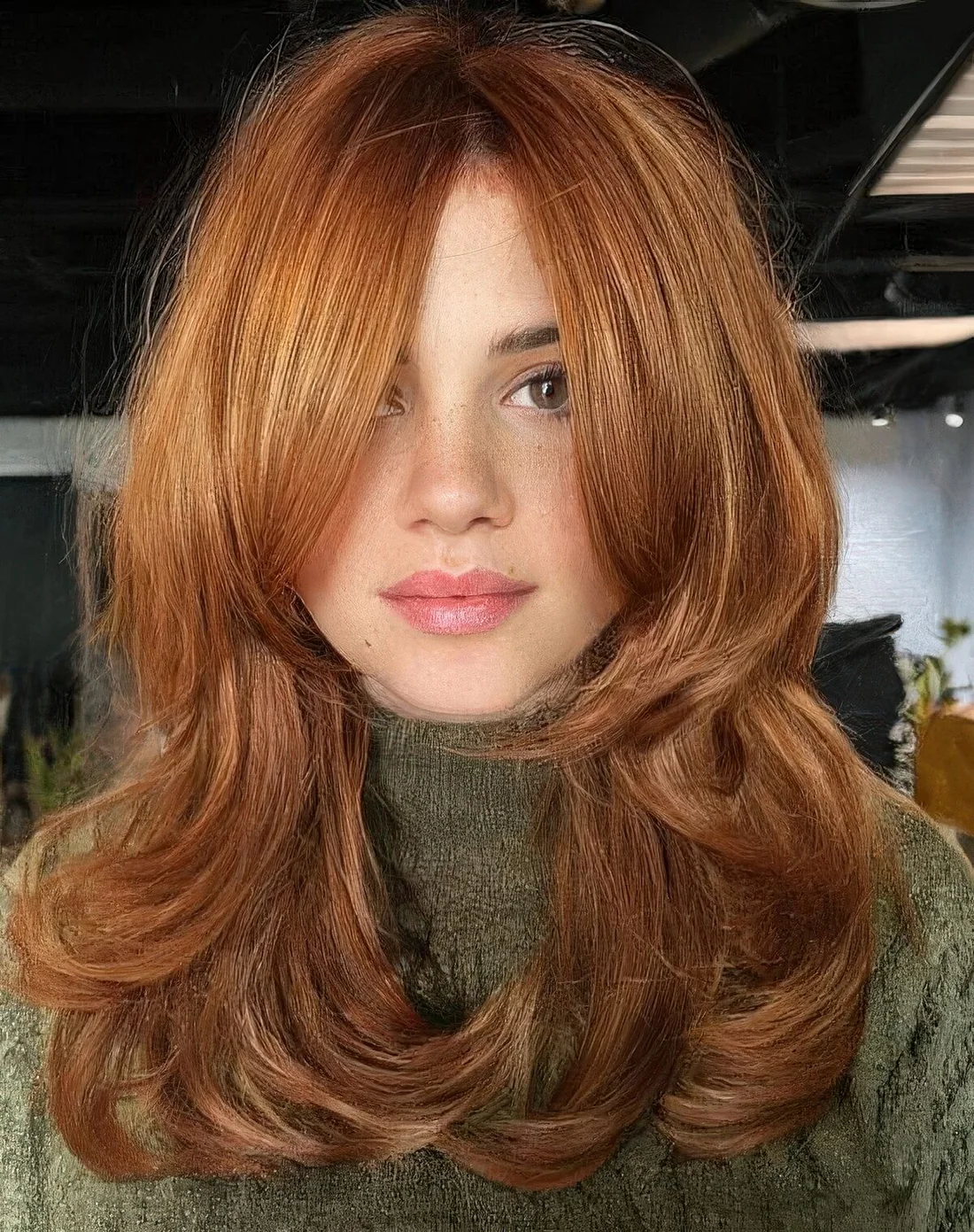 Medium ginger butterfly haircut with bottleneck bangs and curled ends.
