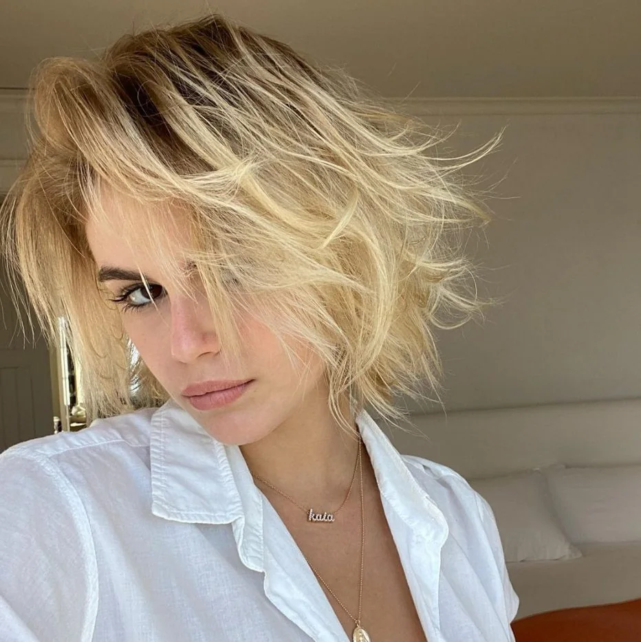 Kaia Gerber wearing a beautiful creamy blonde shade with a darker root and a boy bob haircut with a lot of texture.