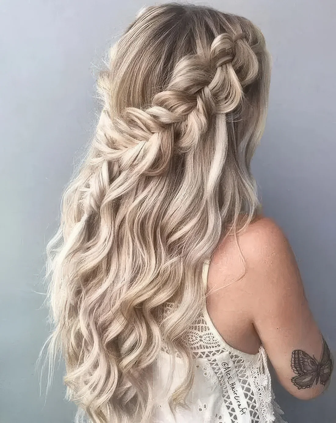 Boho half updo with large loose braids on both sides of the head and waves down.