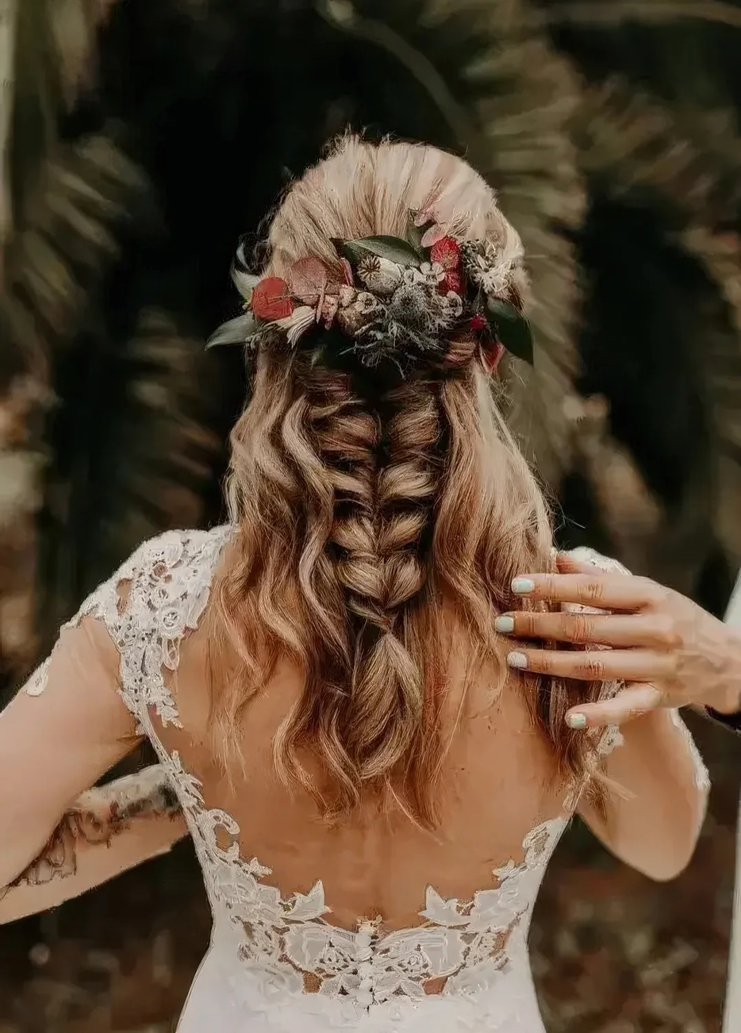 Wedding half updo with locks down and a large and thick braid, with neutral and red blooms for an accent.