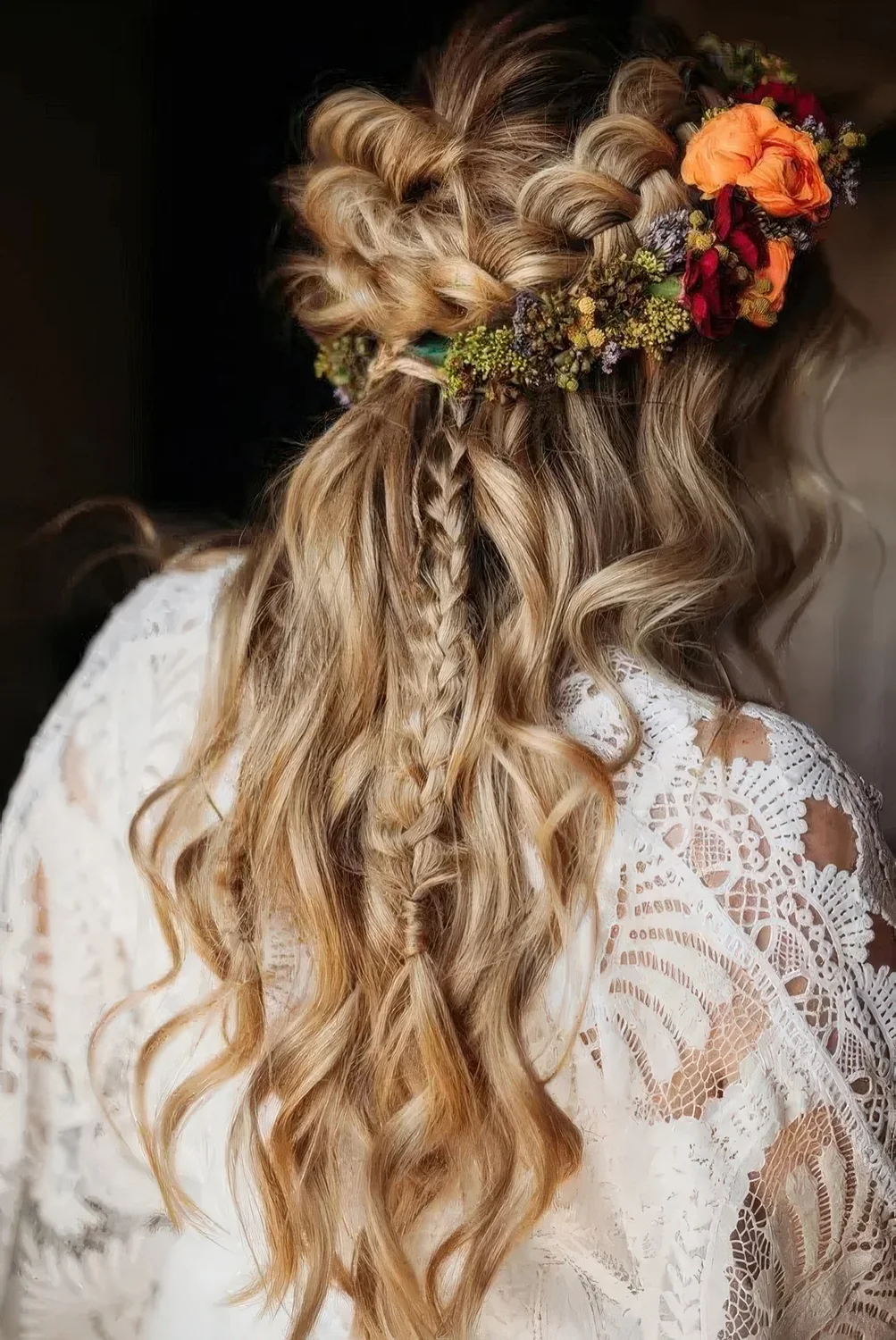 Boho wedding hairstyle with a loose braided halo, a long briad and waves down and some bright blooms.