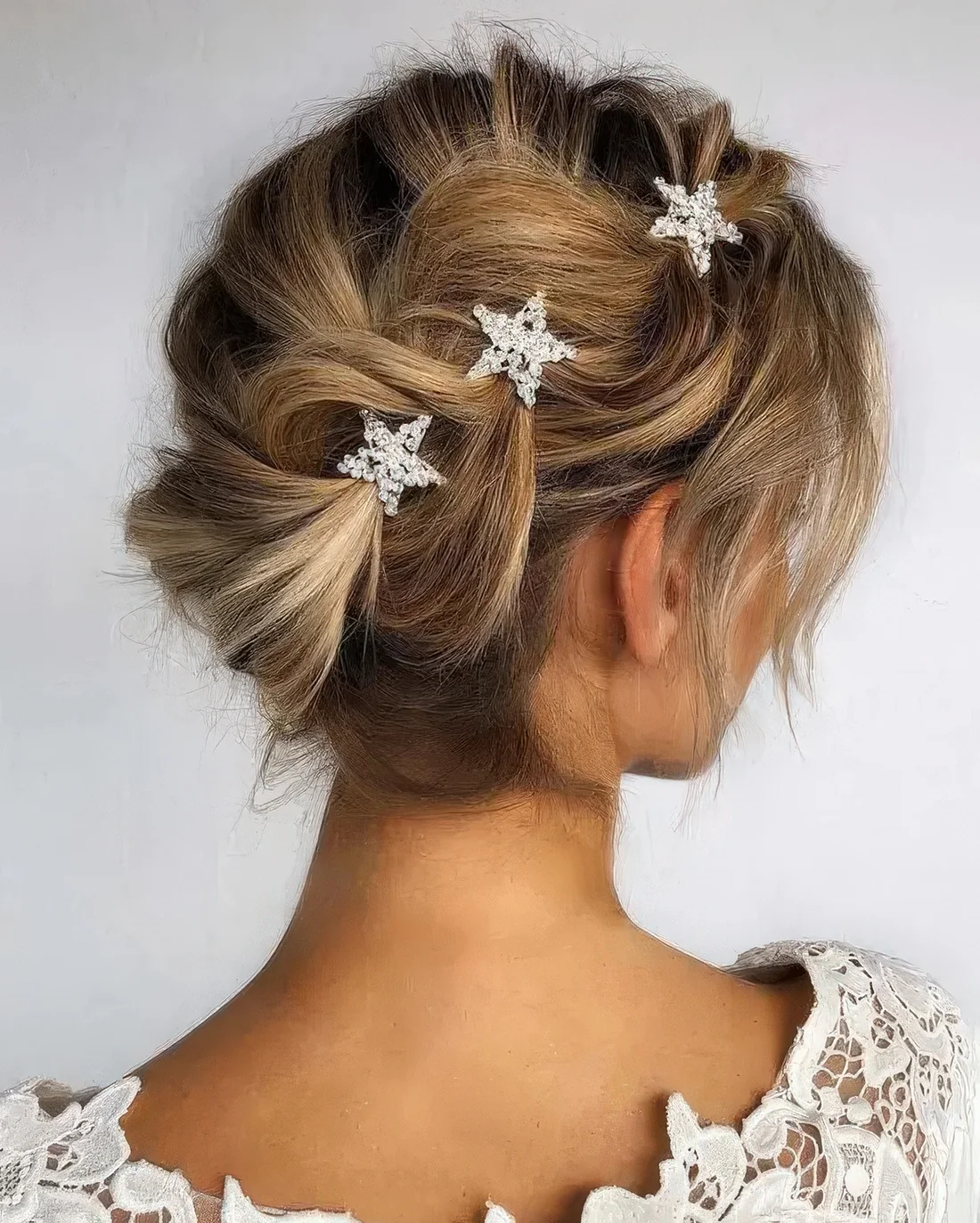 Whimsical updo with a loose braid on one side and star rhinestone hairpins.