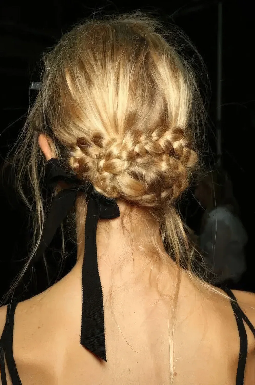 Creative braided low updo with a messy top, some hair down and a black ribbon bow.