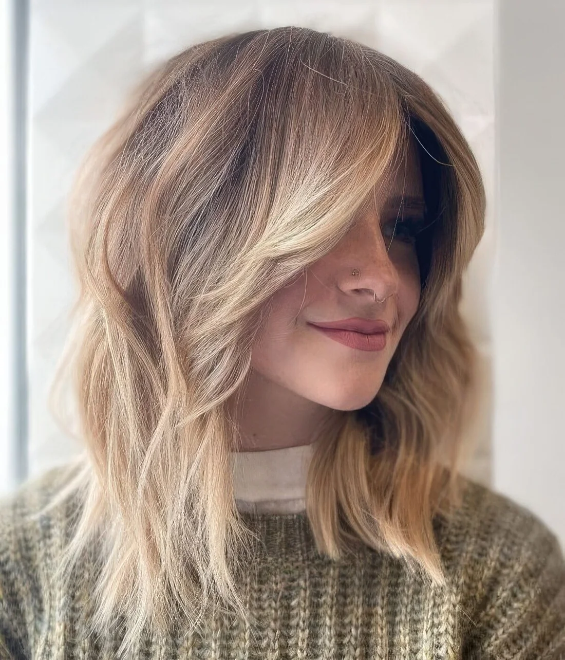 Light brown layered long bob with blonde balayage, a money piece done with an ombre effect and a lot of volume.