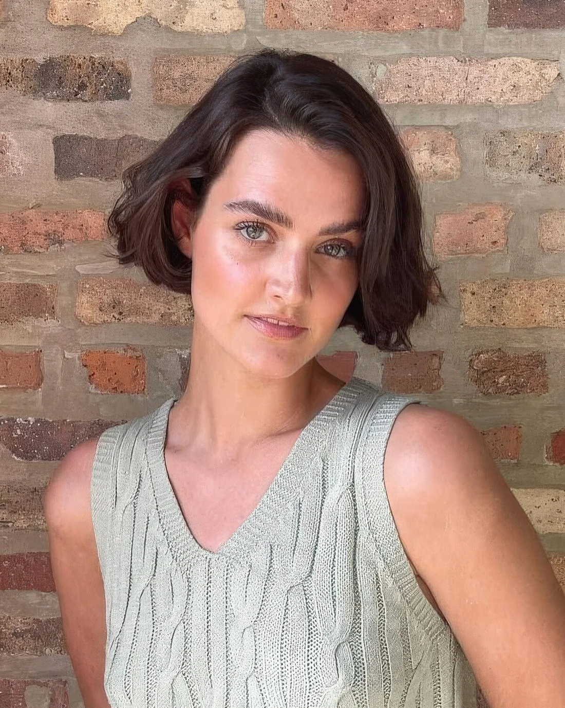 Dark brunette ear-length hairstyle with a messy part and waves.