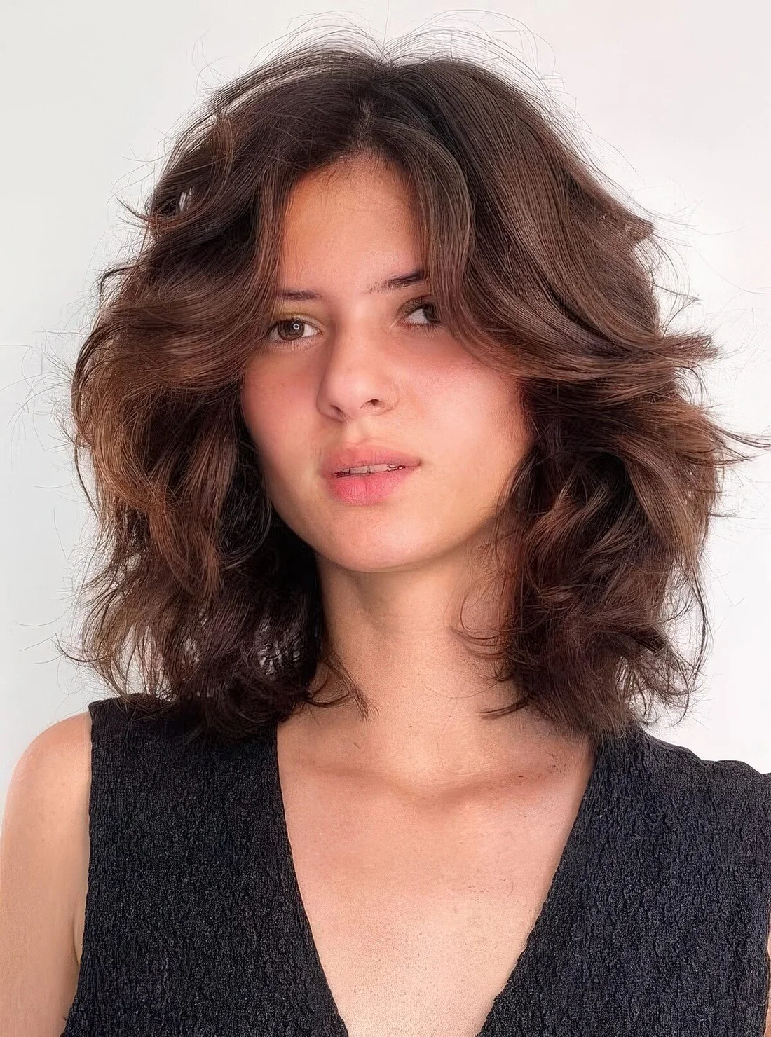 Dark brunette medium-length butterfly haircut on wavy hair, with a lot of dimension.