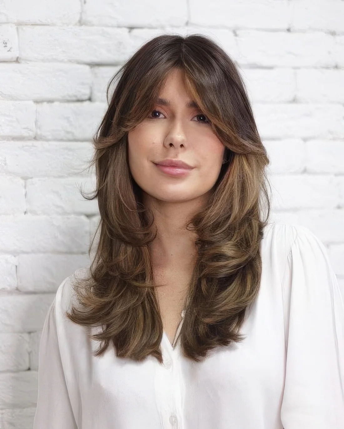 Long brown butterfly haircut with bottleneck bangs and caramel balayage plus curled ends.
