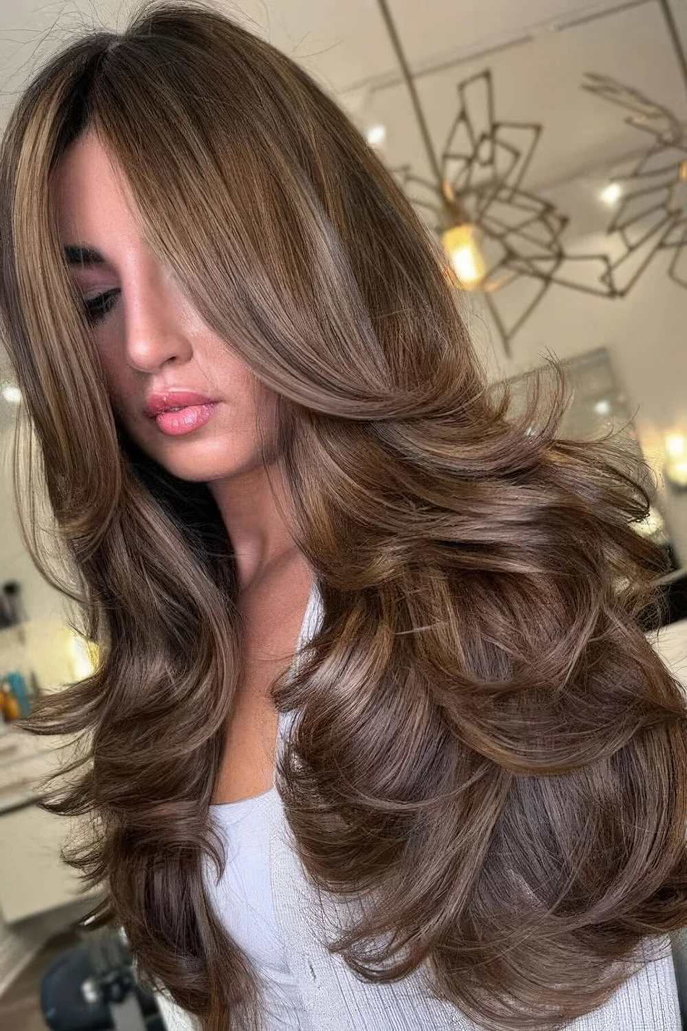 Long brunette butterfly haircut with curtain bangs and a bit of golden blonde balayage.