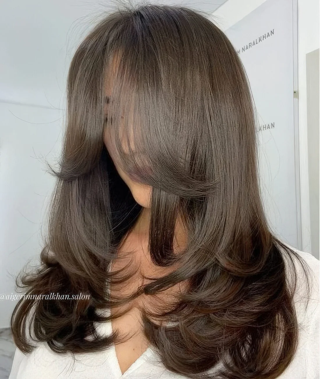 Butterfly haircut on dark brown hair, with layers and curved ends, with curtain bangs.
