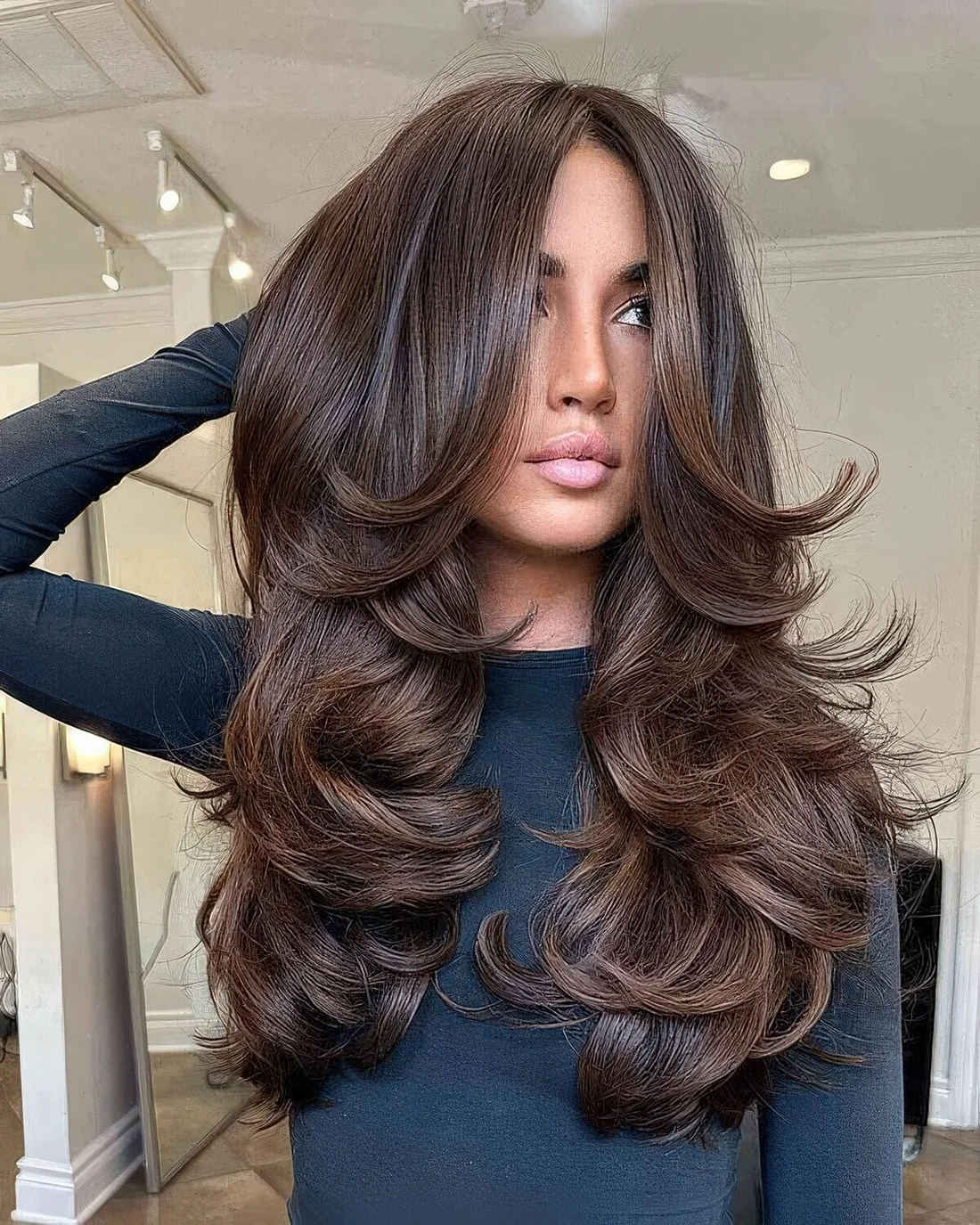 Dark brown butterfly haircut on long hair, with a lot of volume and curtain bangs.