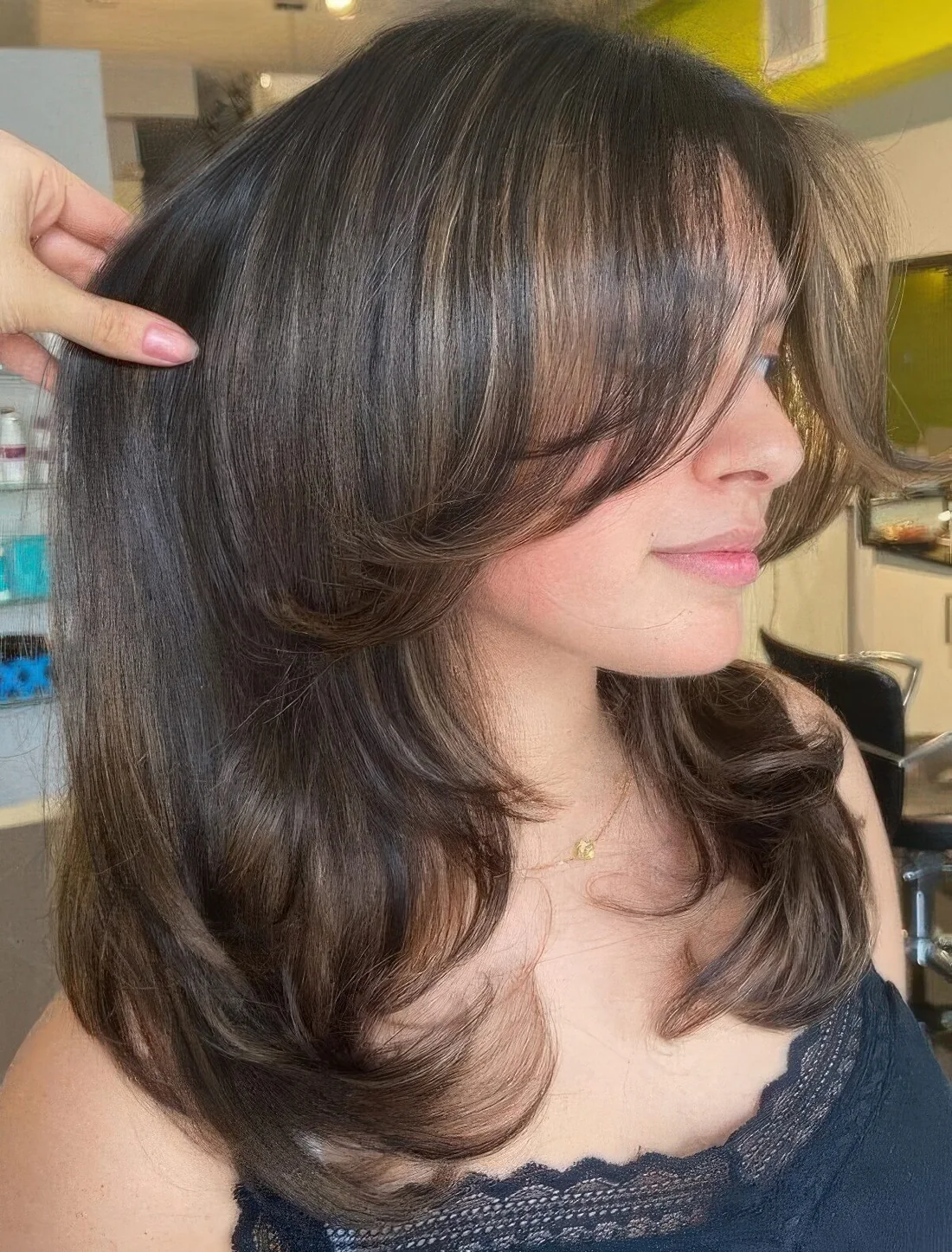 Dark brunette medium butterfly haircut wiht caramel highlights and side bangs plus curved ends.
