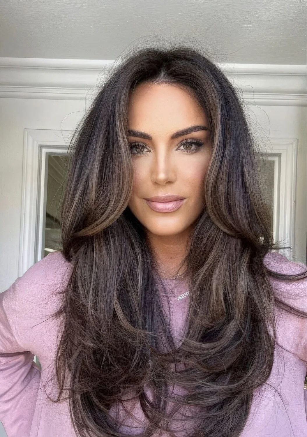 Dark brown butterfly haircut with caramel highlights and long curtain bangs, curled ends and dimension.