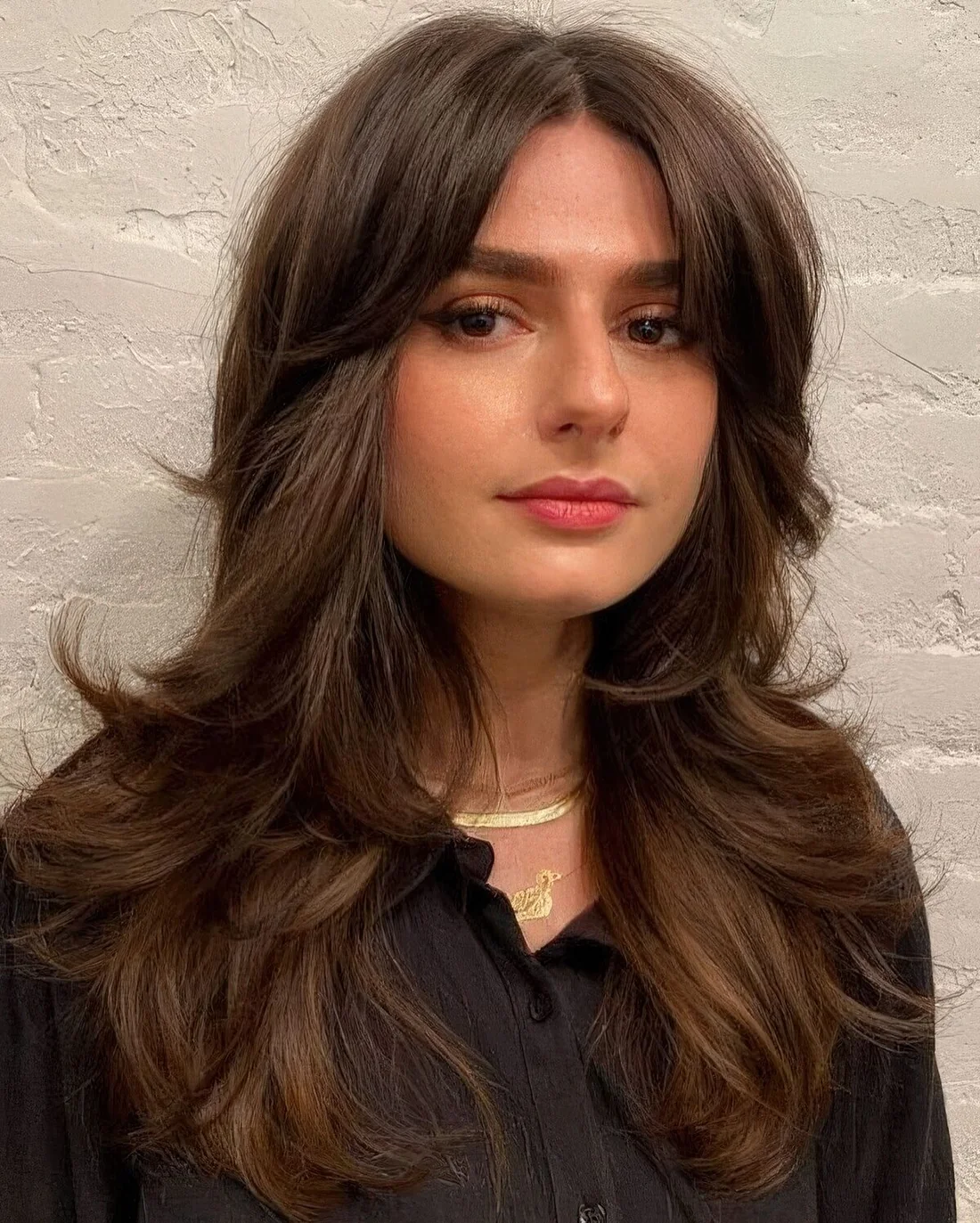 Long brown butterfly haircut with curled ends and short curtain bangs.