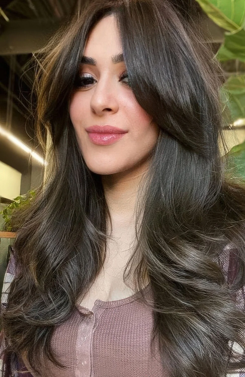 Long brunette butterfly haircut with long curtain bangs and curled ends.