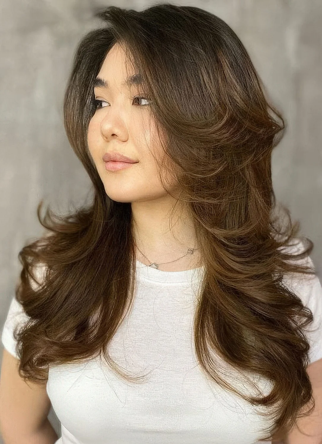 Long dark brunette butterfly haircut with caramel balayage and curled ends plus long curtain bangs.