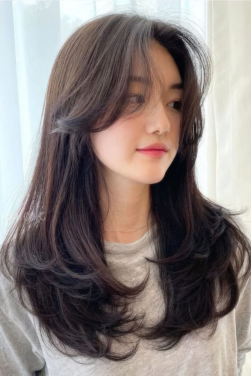 Long dark brunette butterfly haircut with side bangs and curved ends.