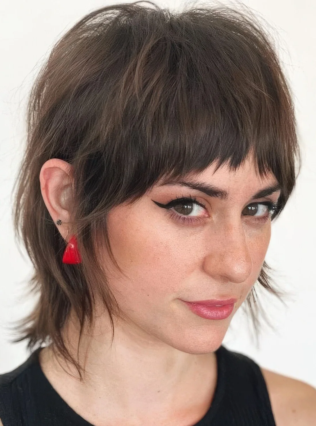 Dark brunette short pixie mullet with bangs, a dimensional crown and shaggy touches.