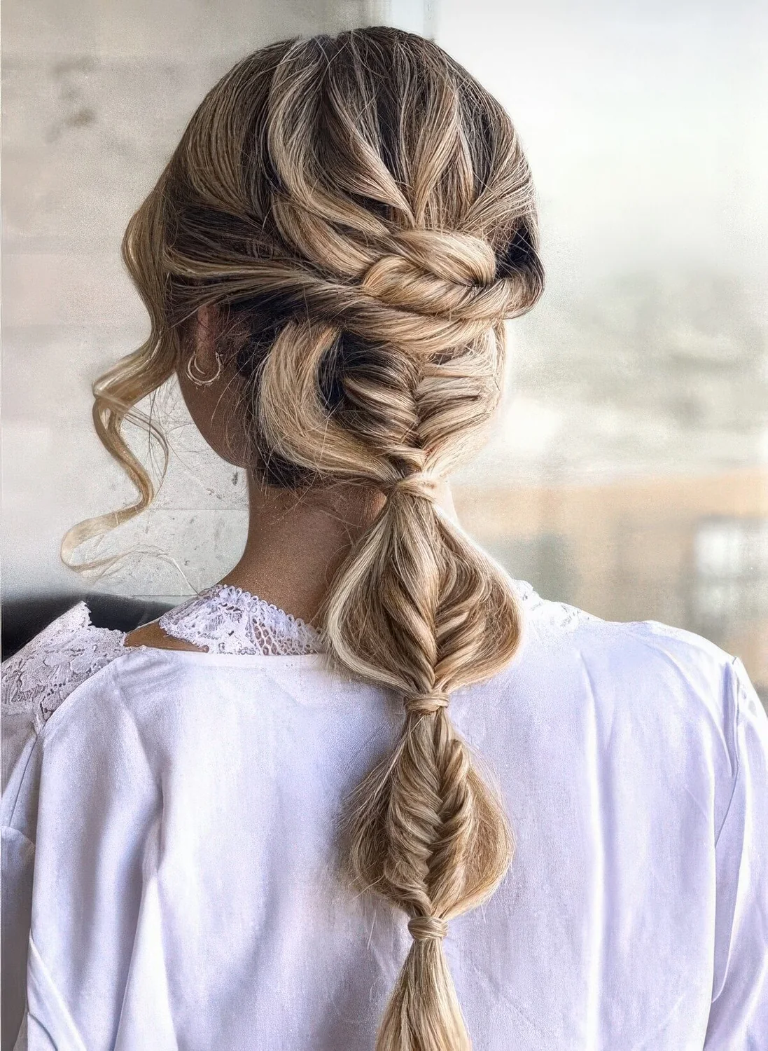 Complicated wedding hairstyle of a fishtail plus bubble low braid, a twisted top and waves framing the face.