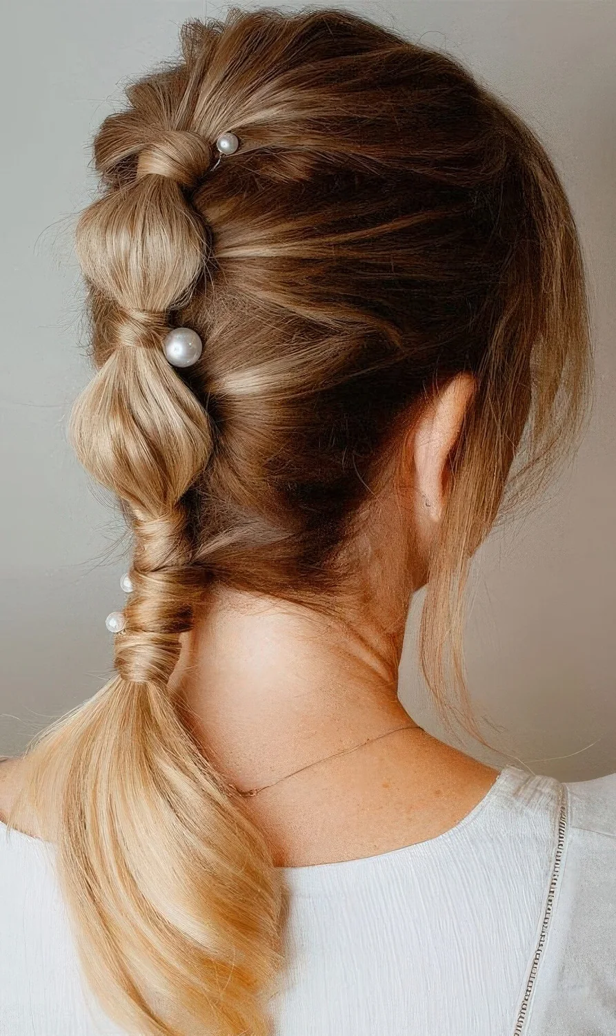 High bubble ponytail attached to the head with pearl hair pins and with a volume on top plus face-framing hair.