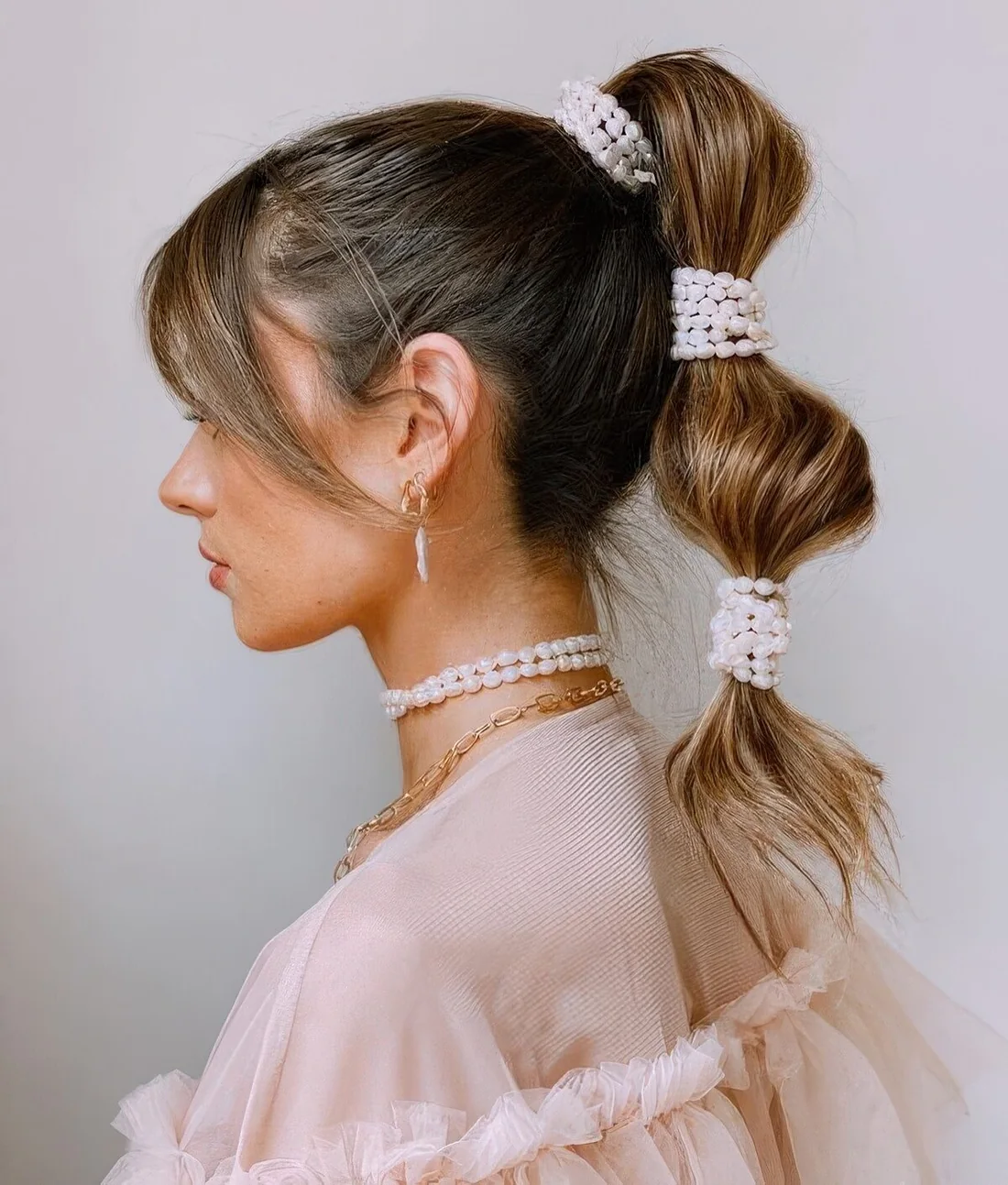 High bubble ponytail with a sleek top and side bangs plus pearl hair elastics.