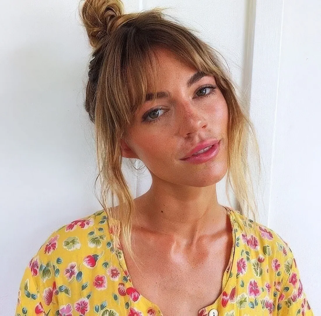 Small messy top knot with layered bangs.
