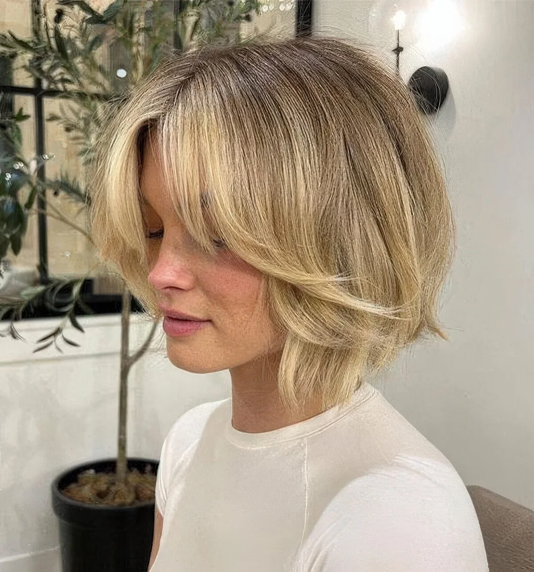 Chin-length blonde butterfly bob with short curtain bangs and razored layers.