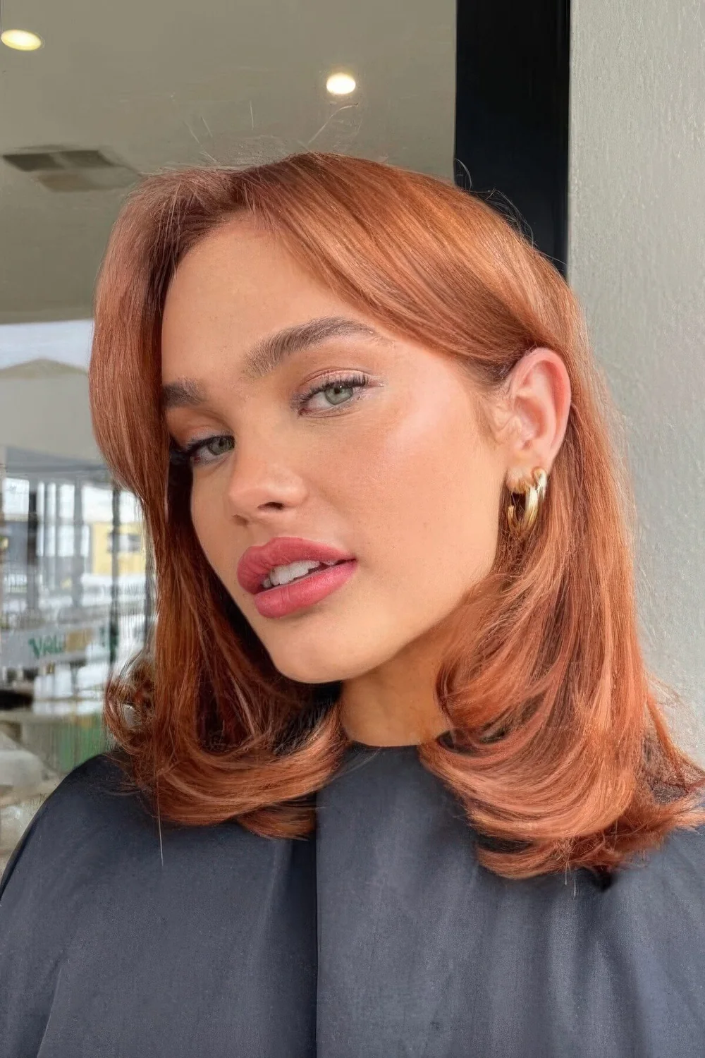 Long ginger red butterfly bob with curtain bangs and curled ends.