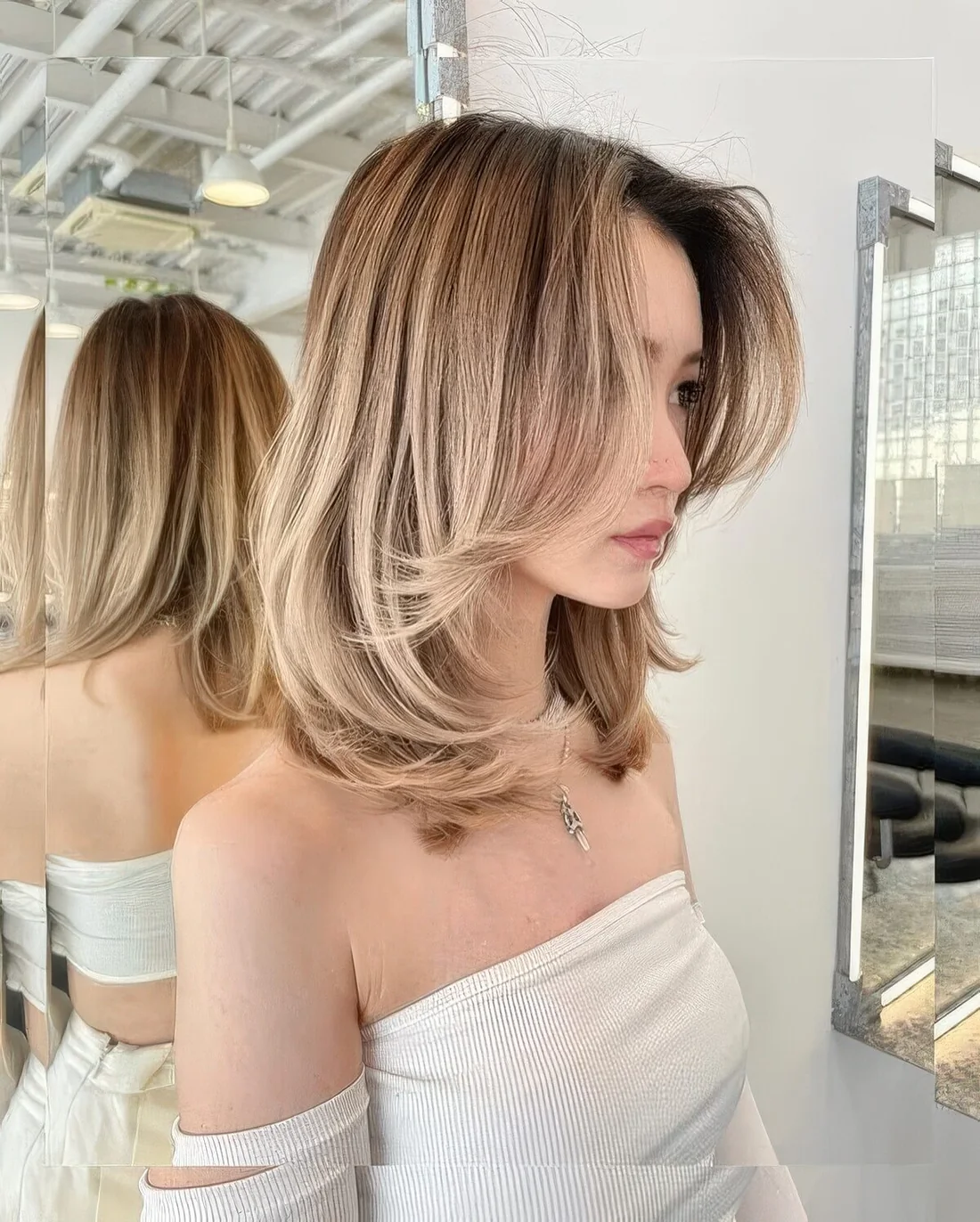 Blonde long butterfly bob with a darker root and curtain bangs plus curled ends for an understated elegance look.