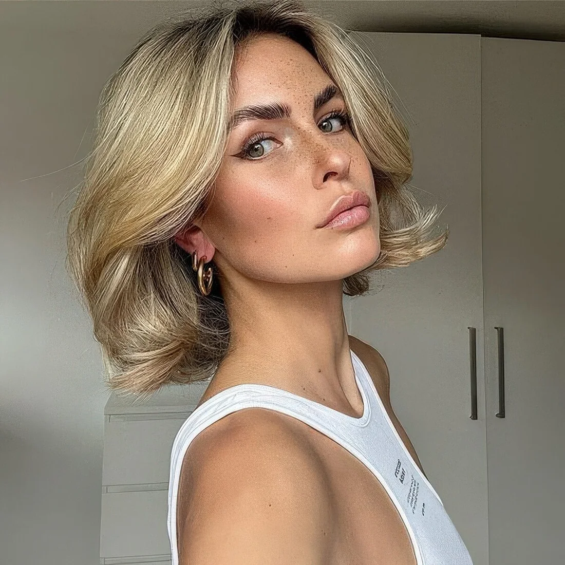 Voluminous golden blonde midi bob with curled ends.