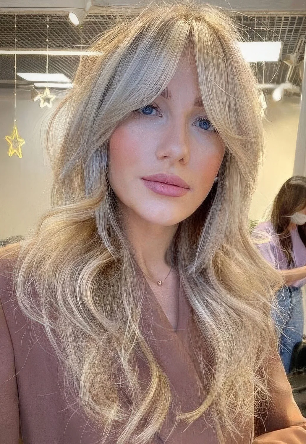 Long blonde butterfly haircut with curtain bangs and waves.