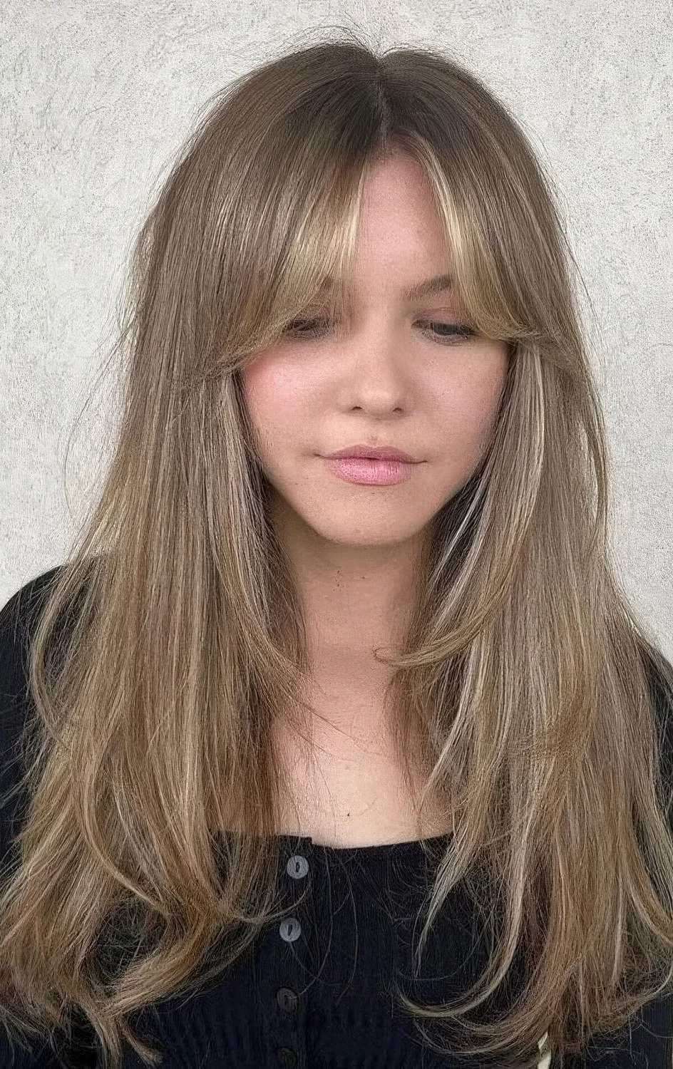 Long bronde butterfly haircut with blonde highlights and curtain bangs.