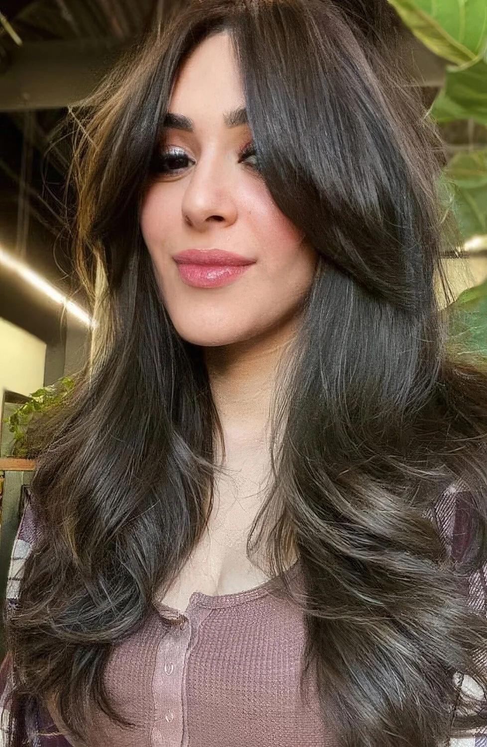 Long brunette butterfly haircut with long curtain bangs and curled ends.