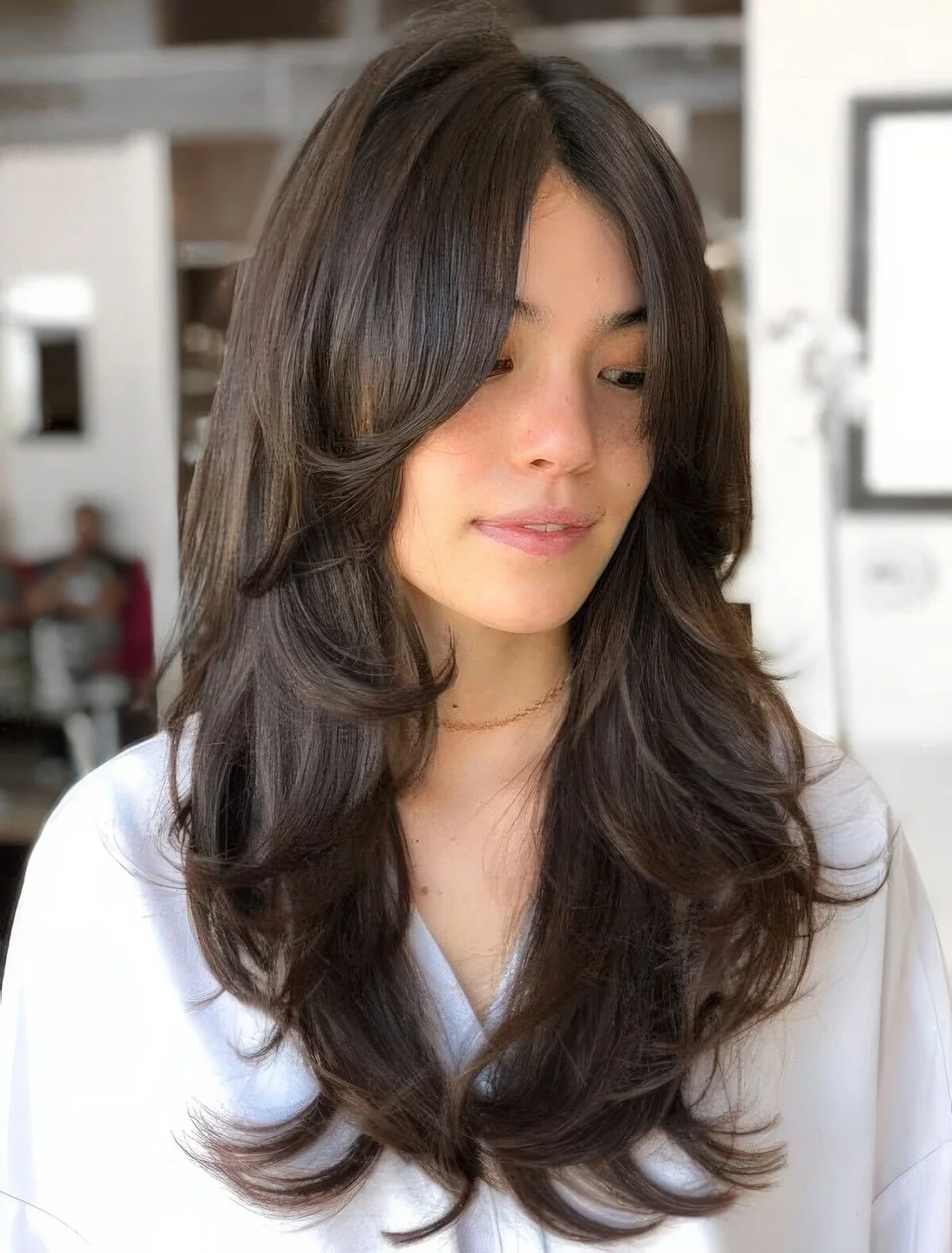 Long dark brown butterfly haircut with curtain bangs and curled ends.