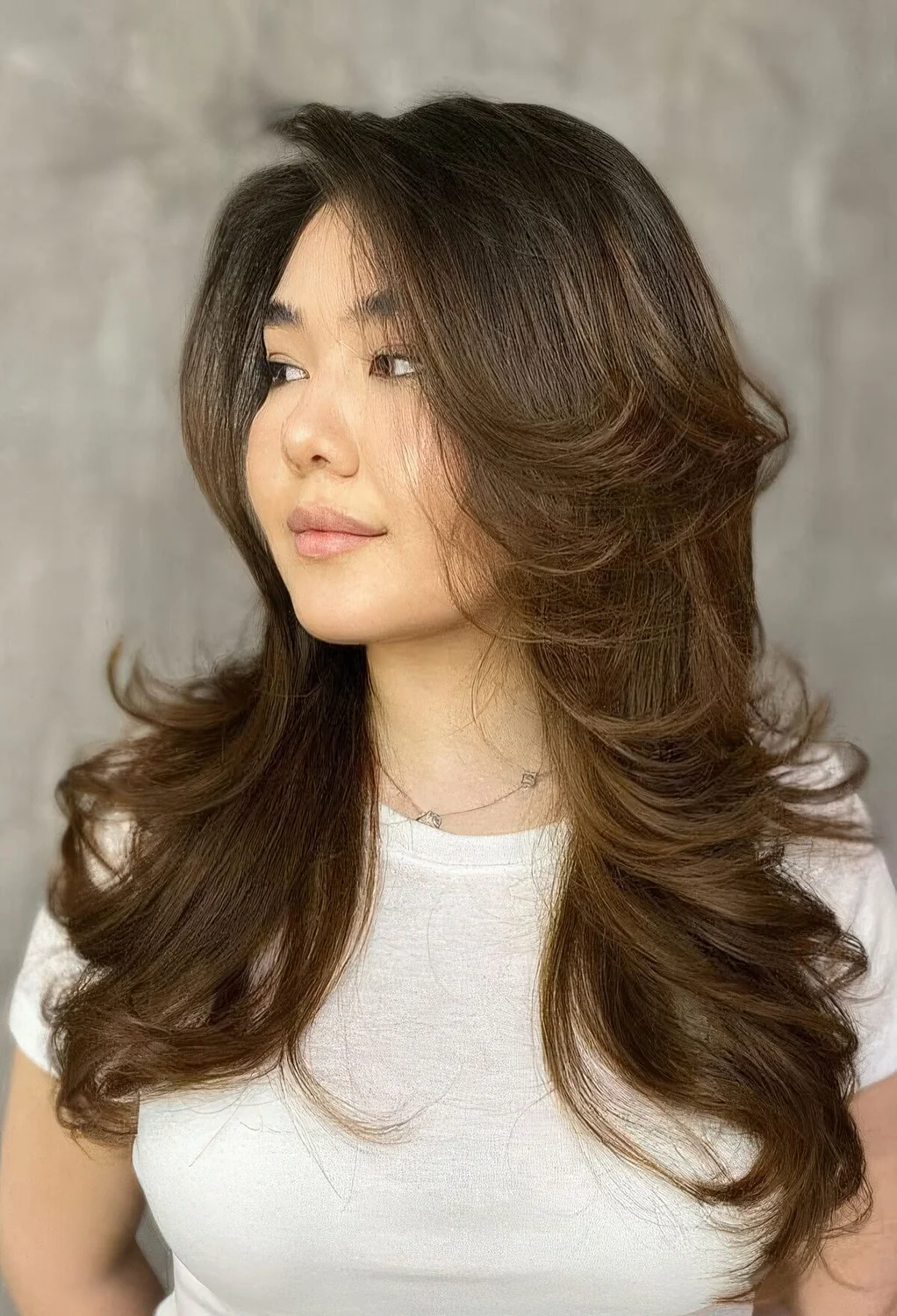 Long dark brunette butterfly haircut with caramel balayage and curled ends plus long curtain bangs.
