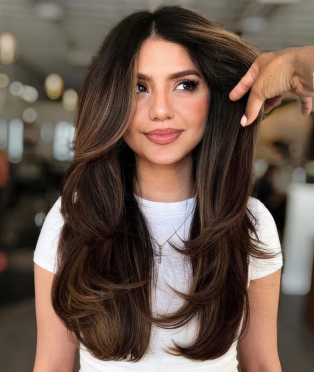 Long dark brunette butterfly haircut with caramel balayage and long curtain bangs plus curled ends.