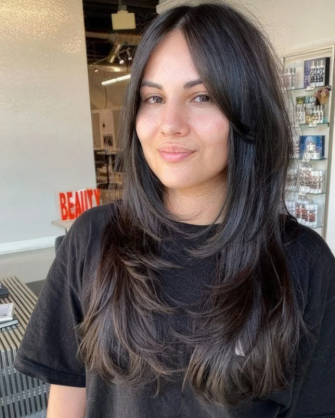 Long dark brunette butterfy haircut with curled ends and long curtain bangs.