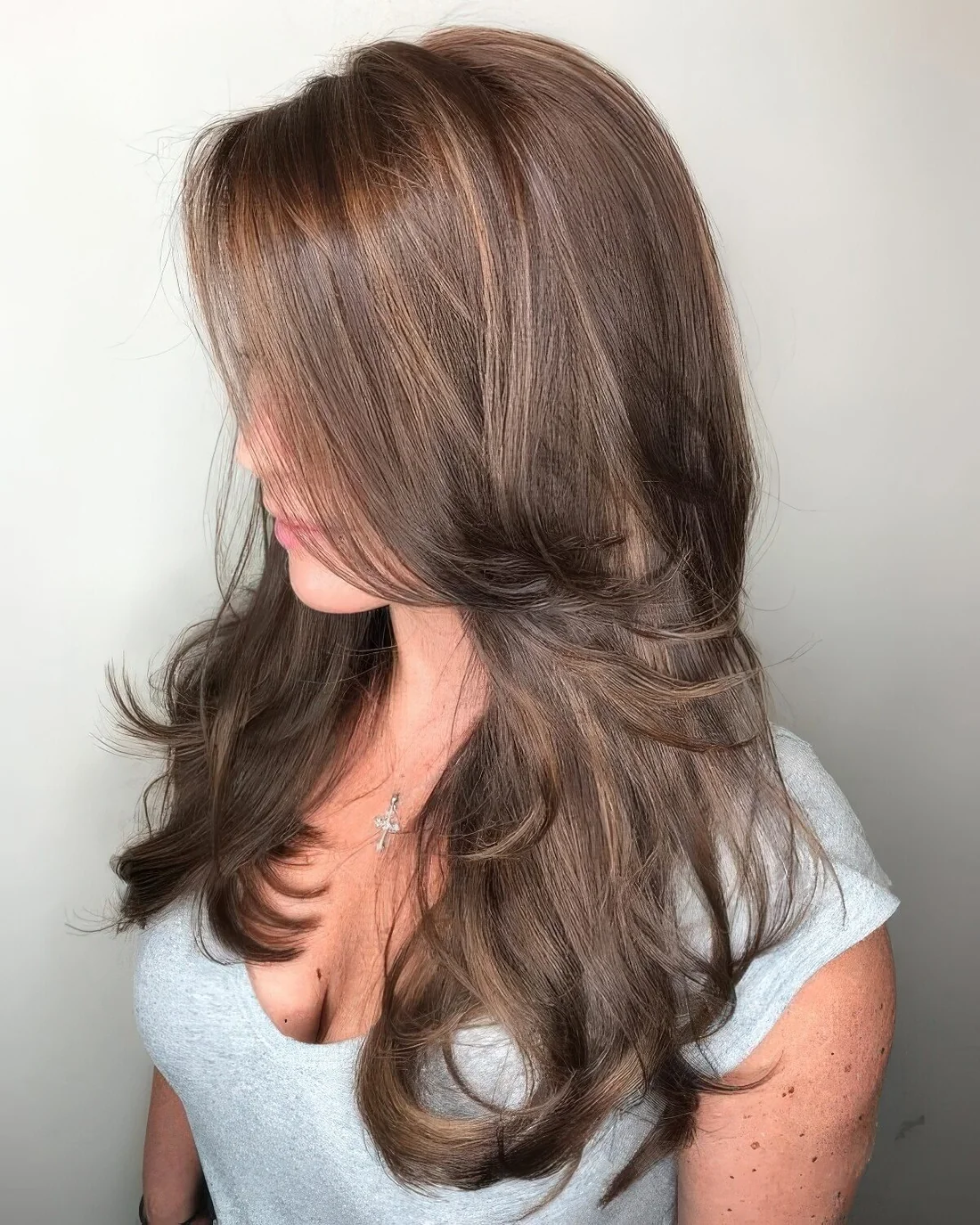 Brunette butterfly haircut with curled ends and long curtain bangs.