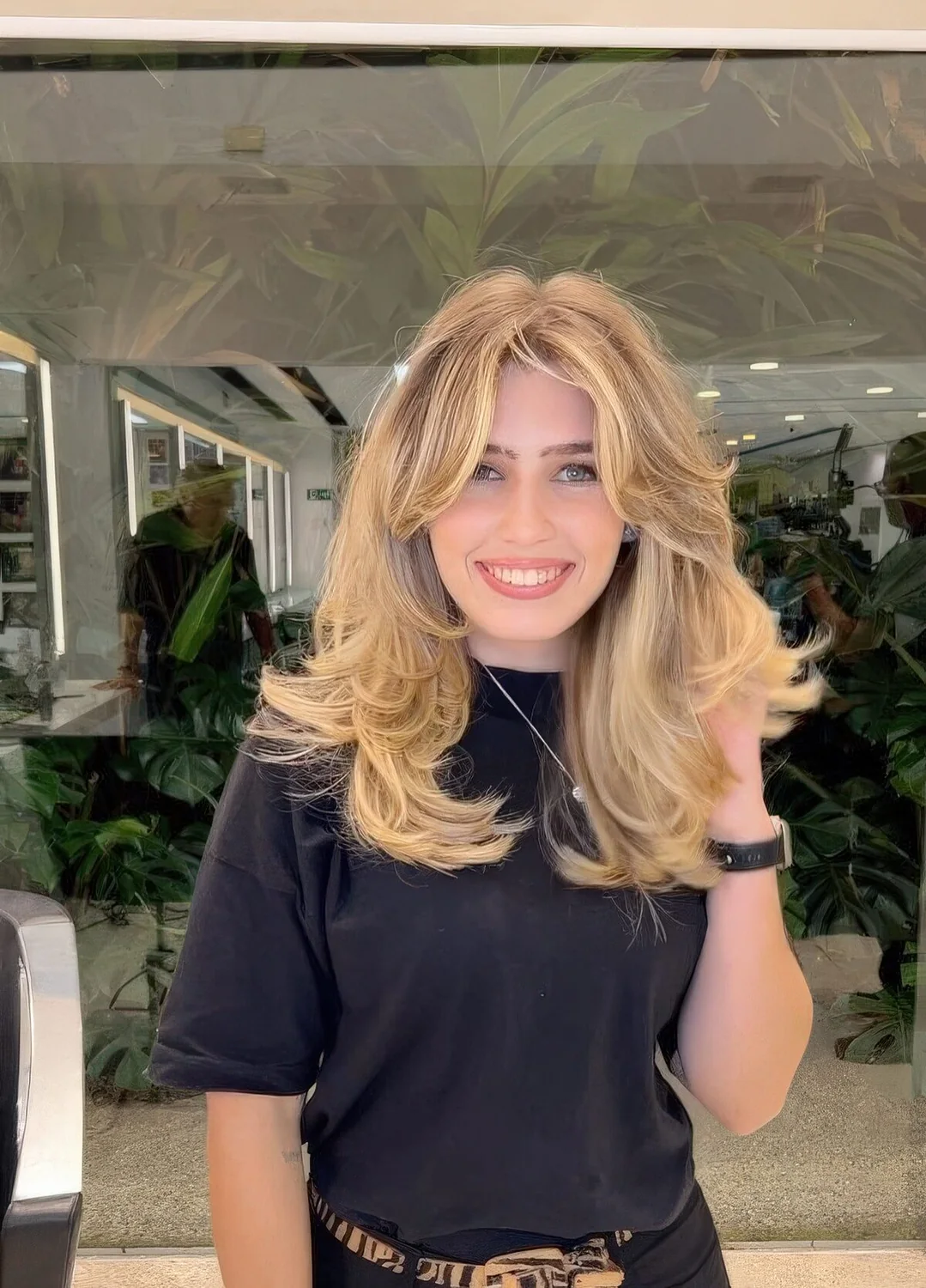 Voluminous blonde butterfly haircut with curtain bangs, wavy ends and a lot of dimension.