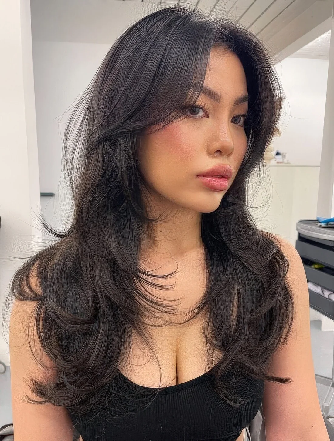 Dark brunette butterfly haircut with curled ends, curtain bangs and some volume.